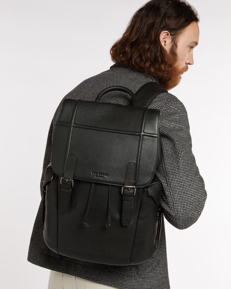 Ein bärtiger Mann, der ein Modell eines Herrenrucksacks aus Leder für die Arbeit trägt