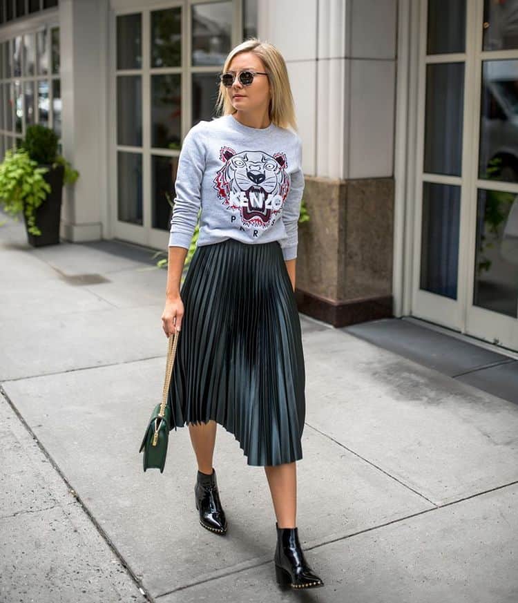 Frau, die ein graues Sweatshirt mit einem plissierten Rock und Stiefeletten trägt