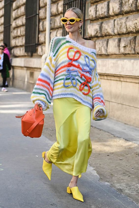 Femme qui porte une malle tricotée par dessus une robe dans la rue.